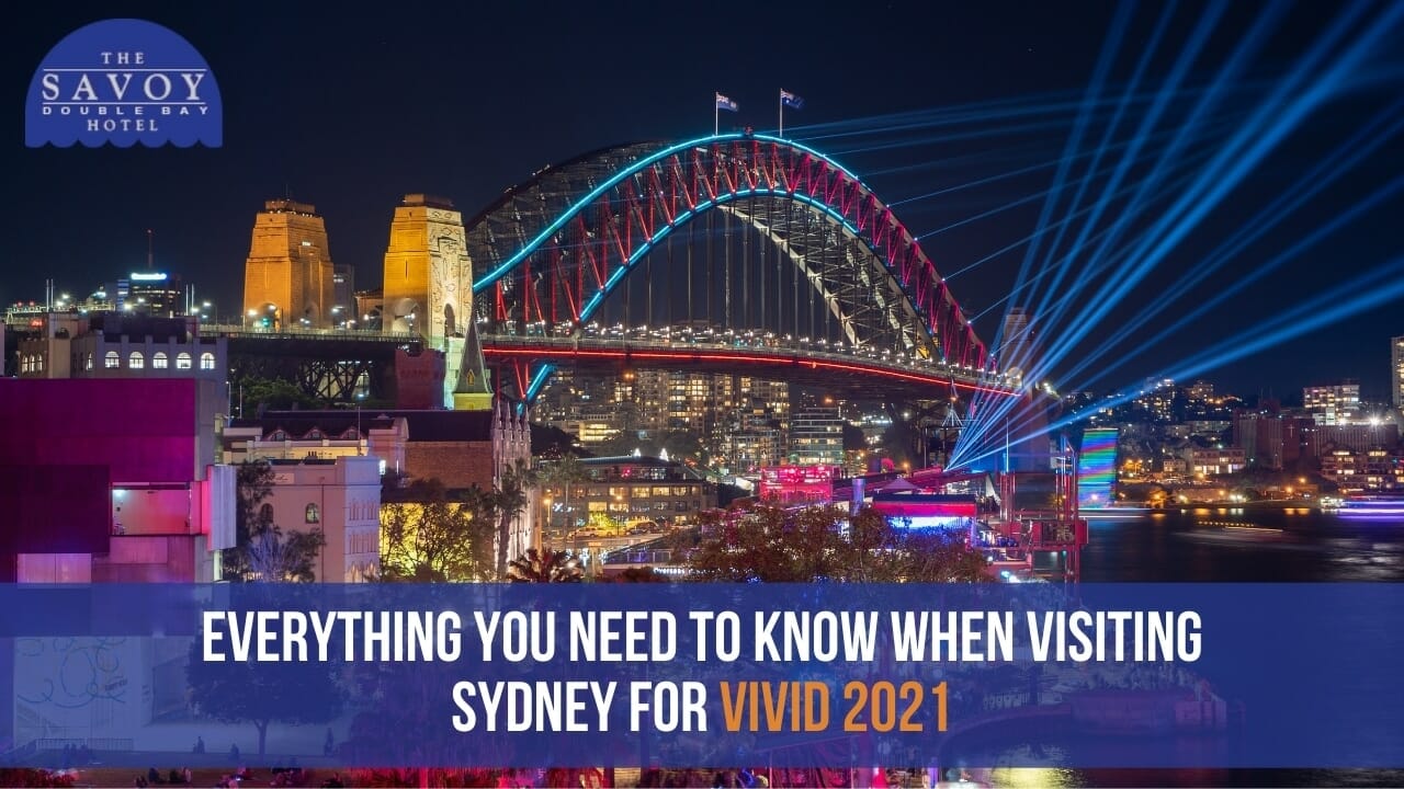 A night shot of the Sydney Harbour Bridge brightly illuminated with red and blue light installations and projecting laser beams into the sky.