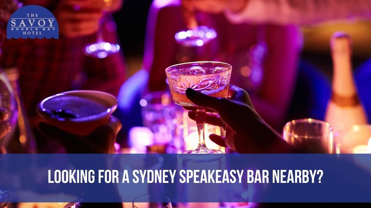 A close-up shot of hands raising cocktail glasses for a toast in a bar illuminated by vibrant purple lighting.