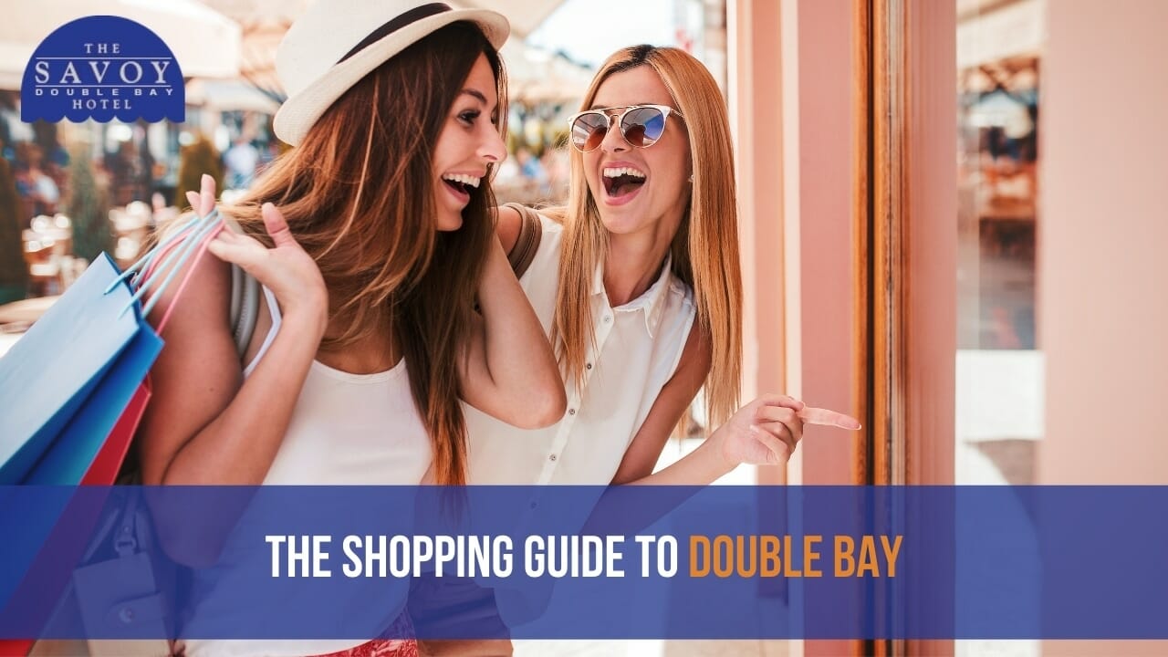 Two smiling young women holding shopping bags laugh together while looking at a storefront window display.