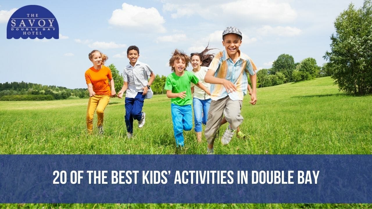 A group of energetic, smiling children running joyfully across a grassy green field under a blue sky.