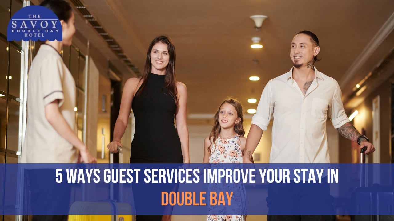 A family consisting of a man, a woman, and a young girl walking down a hotel hallway with rolling suitcases while being greeted by a staff member.