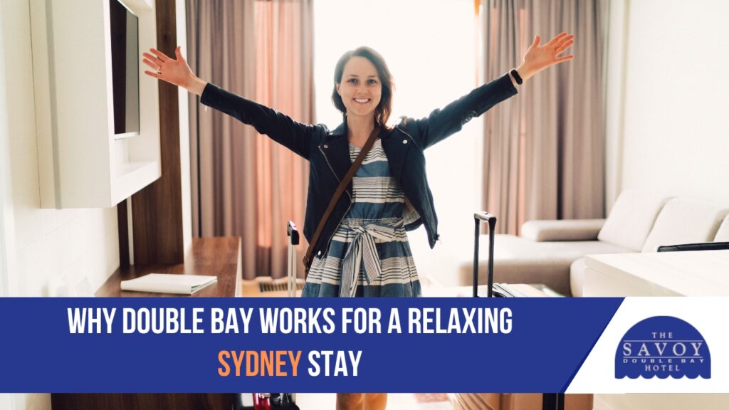 Experience the Art of Slow Travel at Double Bay Hotel - Double Bay A smiling woman stands in a hotel room with her arms outstretched next to her luggage.