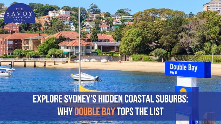 A sunny view of Double Bay beach with boats moored in blue water and hillside residential homes in the background.