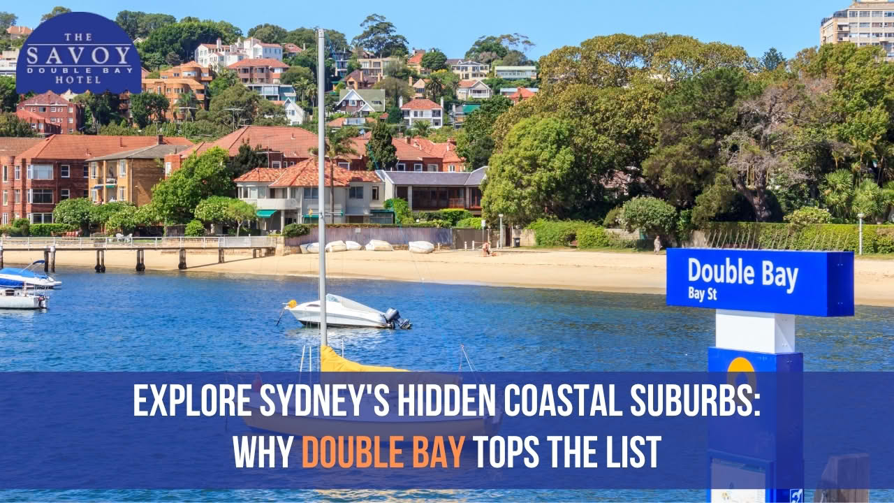 A sunny view of Double Bay beach with boats moored in blue water and hillside residential homes in the background.